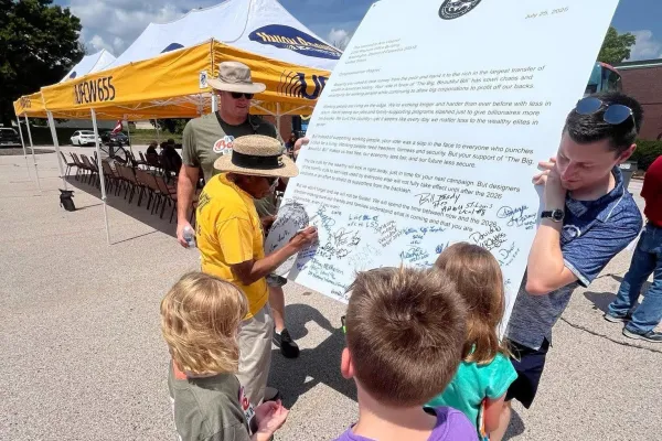 Community members, kids, signing a large letter addressed to their representative